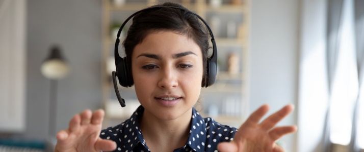 A woman with headphones is presenting to her laptop