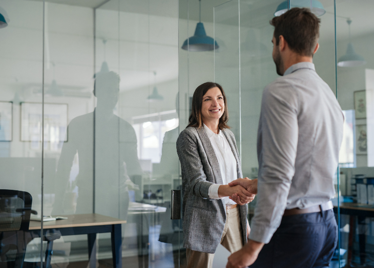 A woman is shaking a mans hand in an office setting