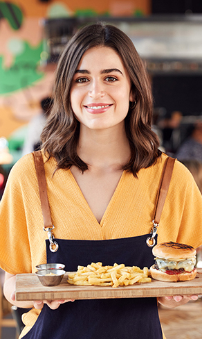 A waitress with a burger and chips on a wooden platter