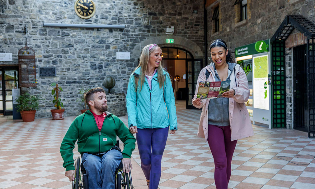 Three individuals, two women and one man in a wheelchair, walking through Belvedere House. They are engaged in looking at a map.