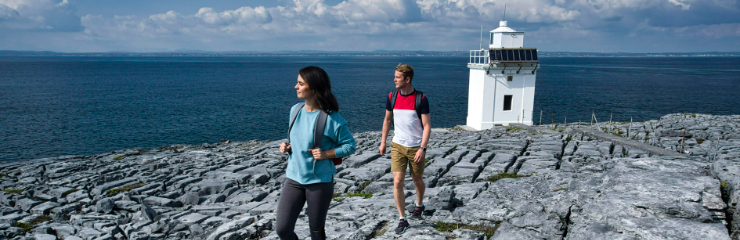 A couple walking through the burren and a lighthouse is in the background