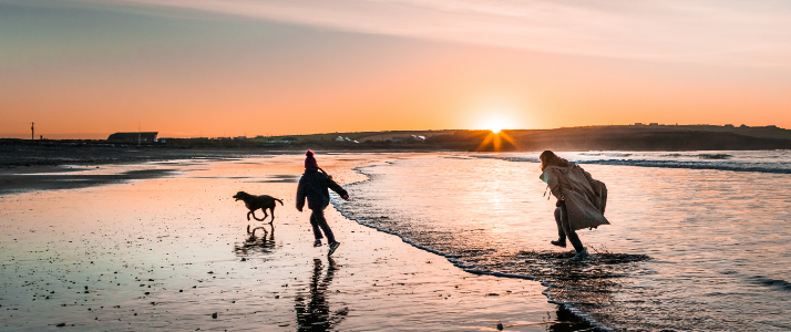 A mother walking with her child on the beach as the sun is setting