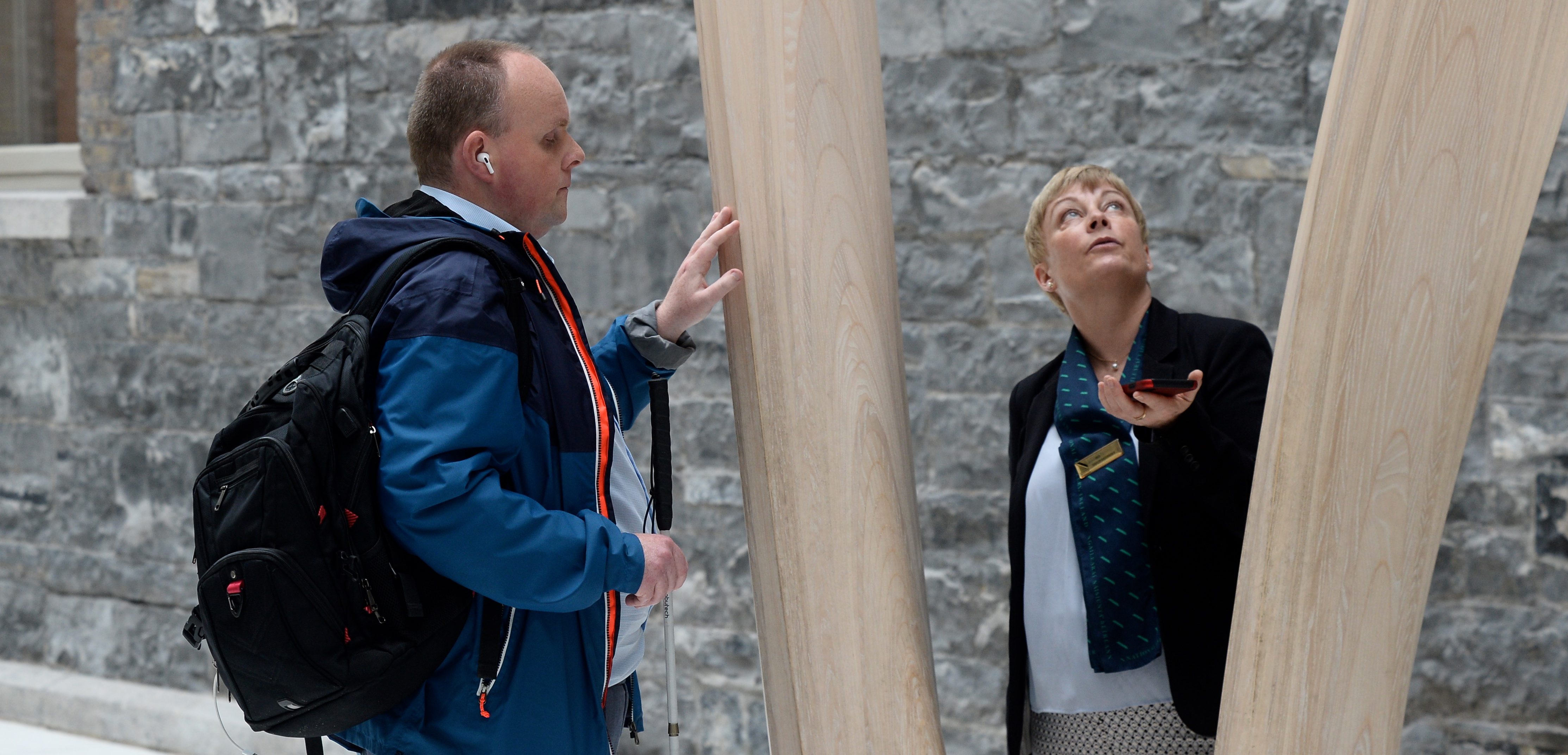 Man with a walking stick in museum touching sculpture