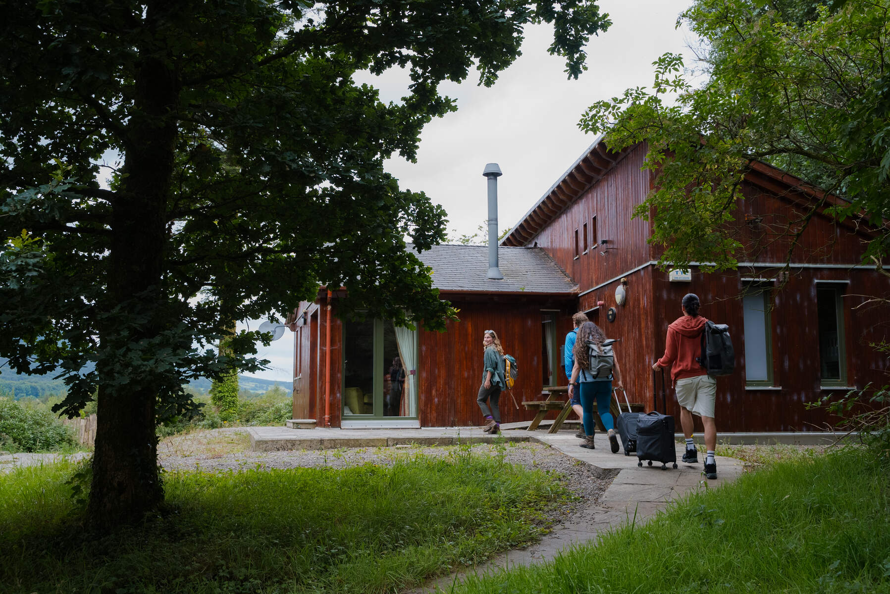 3 people with bags walking towards a wooden lodge in the woods