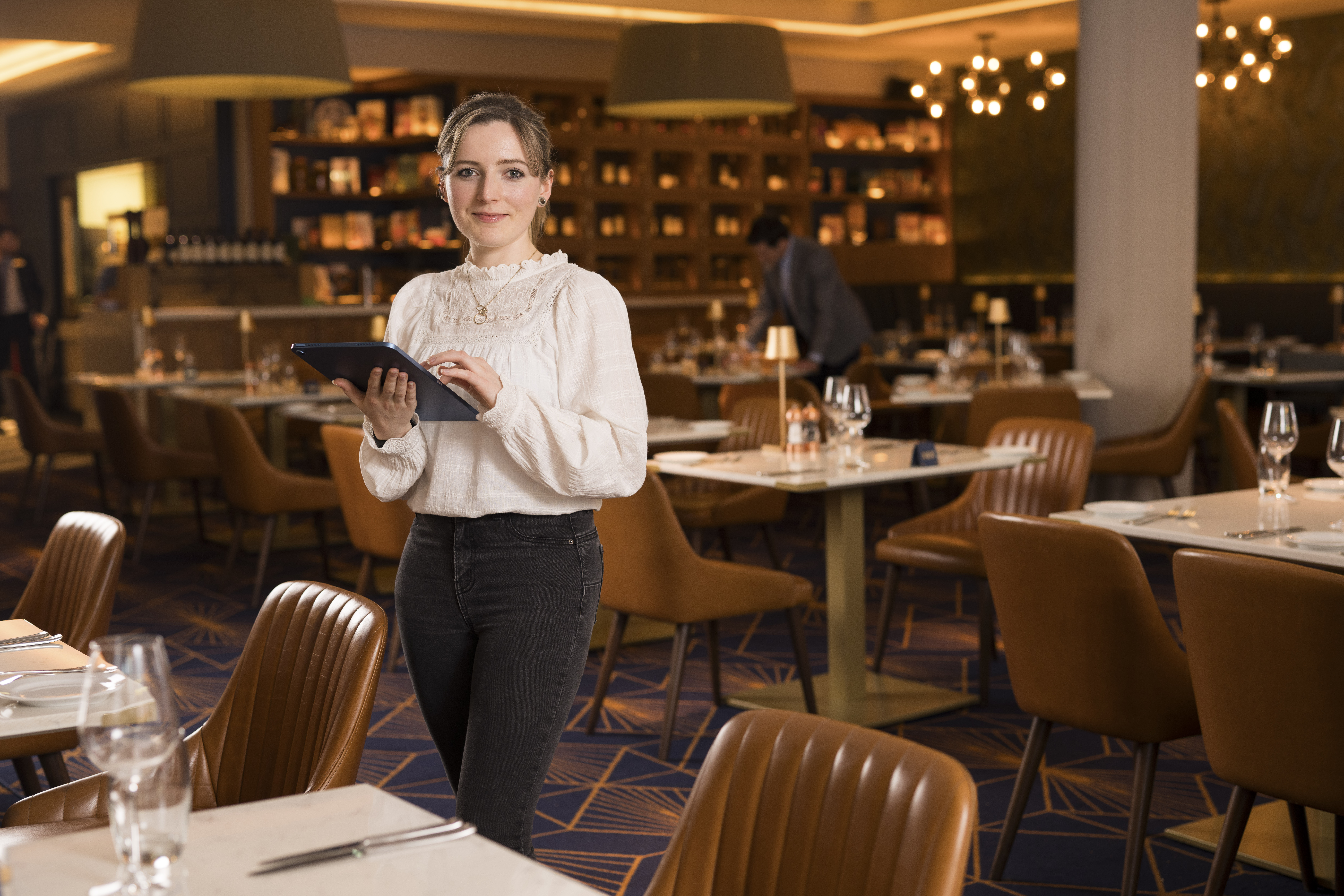 Woman working in hospitality holding tablet and standing by restaurant table