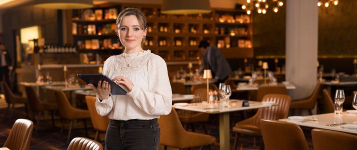 Woman working in hospitality holding tablet and standing by restaurant table