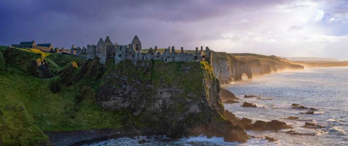 Green cliffs with ruins at sunset. The sea below foams with waves.