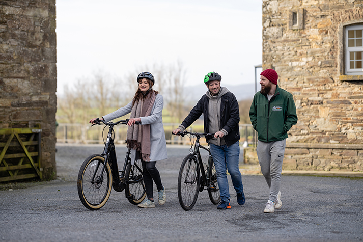 Three people walking, two of them are walking with bikes